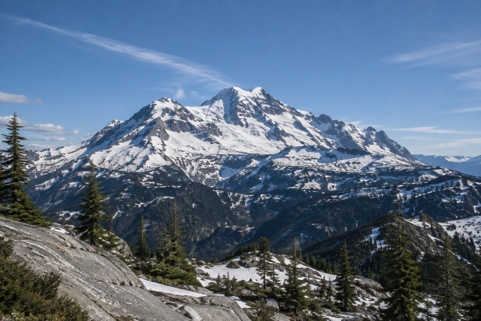 Snow-covered mountain range rising above evergreen forest and rocky alpine terrain